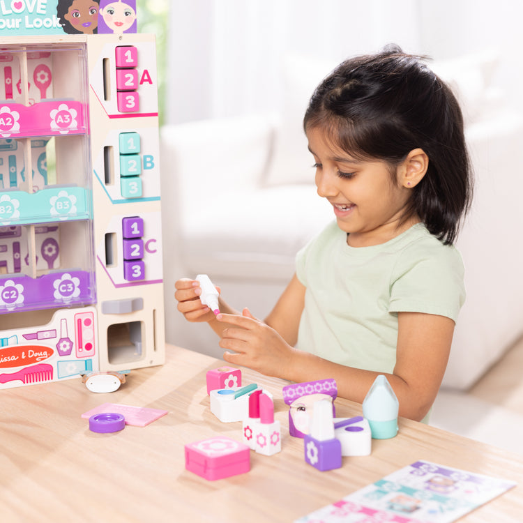A kid playing with The Melissa & Doug Sort, Stock, Select Beauty Kiosk Vending Machine Play Set, Pretend Makeup Wooden Toy For Boys and For Girls 3+