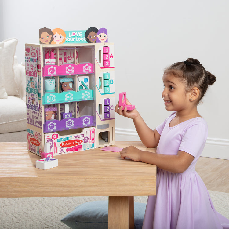 A kid playing with The Melissa & Doug Sort, Stock, Select Beauty Kiosk Vending Machine Play Set, Pretend Makeup Wooden Toy For Boys and For Girls 3+