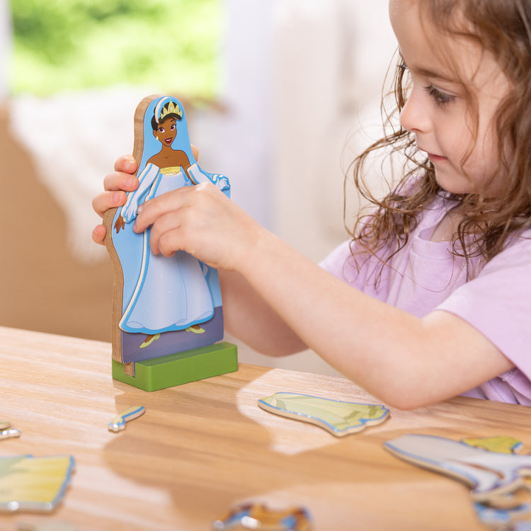 A kid playing with The Melissa & Doug Disney Princess Tiana Magnetic Dress-Up Wooden Doll Pretend Play Set (30+ pcs)
