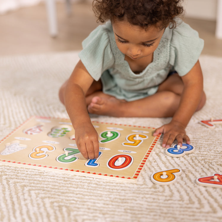 A kid playing with The Melissa & Doug Lift & See Numbers Wooden Peg Puzzle - 10 Pieces