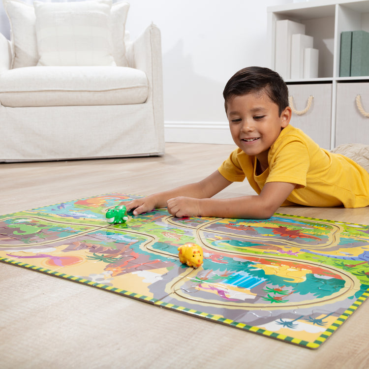 A kid playing with The Melissa & Doug Dinosaur Adventure Tracks Cardboard Jigsaw Floor Puzzle and 2 Wind-Up Dinos – 48 Pieces, for Boys and Girls 3+ 