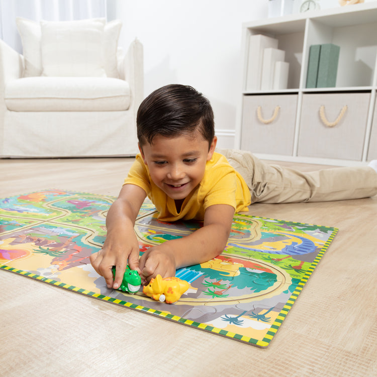A kid playing with The Melissa & Doug Dinosaur Adventure Tracks Cardboard Jigsaw Floor Puzzle and 2 Wind-Up Dinos – 48 Pieces, for Boys and Girls 3+ 