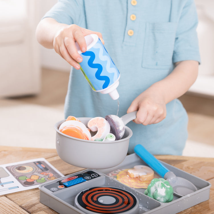 A kid playing with The Melissa & Doug Simmer & Stir Stovetop Play Set with Water WOW!® Color Changing Play Food Preschool Toy Ages 3+
