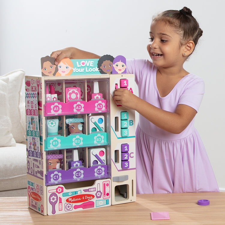 A kid playing with The Melissa & Doug Sort, Stock, Select Beauty Kiosk Vending Machine Play Set, Pretend Makeup Wooden Toy For Boys and For Girls 3+