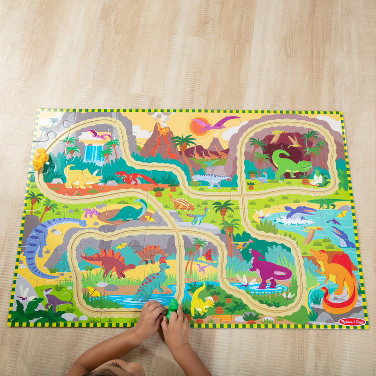 A kid playing with The Melissa & Doug Dinosaur Adventure Tracks Cardboard Jigsaw Floor Puzzle and 2 Wind-Up Dinos – 48 Pieces, for Boys and Girls 3+ 