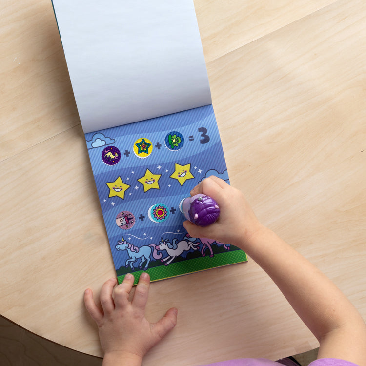 A kid playing with The Melissa & Doug Sticker WOW!™ 24-Page Activity Pad and Sticker Stamper, 300 Stickers, Arts and Crafts Fidget Toy Collectible Character – Sprinkles the Purple Unicorn
