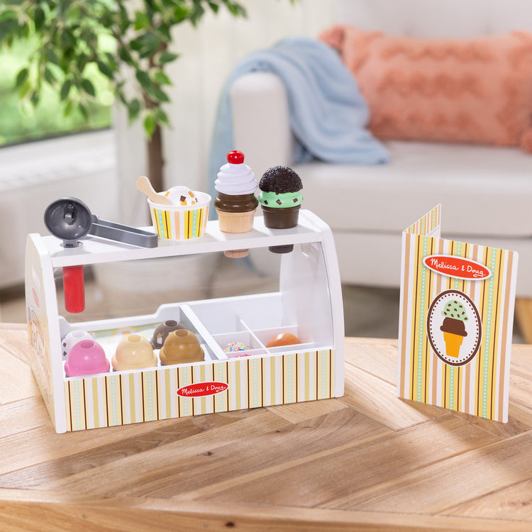 A kid playing with The Melissa & Doug Wooden Scoop and Serve Ice Cream Counter With Play Food and Accessories (28 Pcs) 